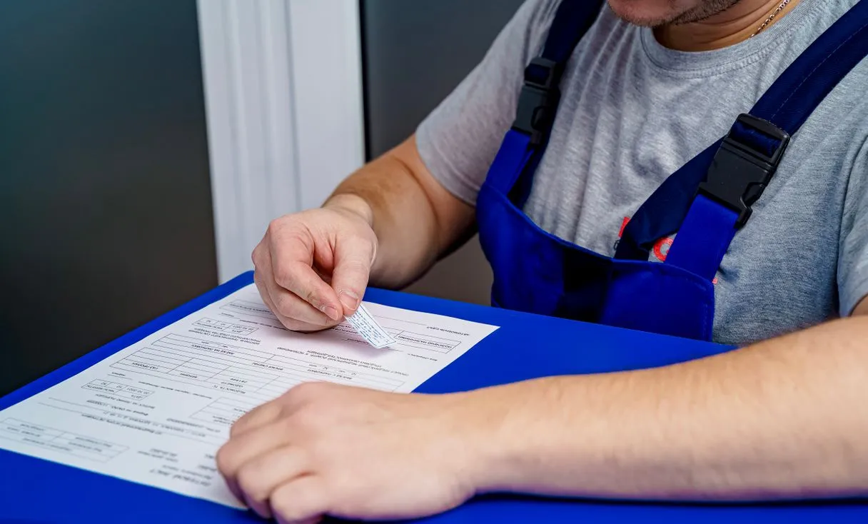 Técnico de uniforme preenchendo um documento na bancada representando: Nota Fiscal na Assistência Técnica: quando emitir e como separar serviço de peça
