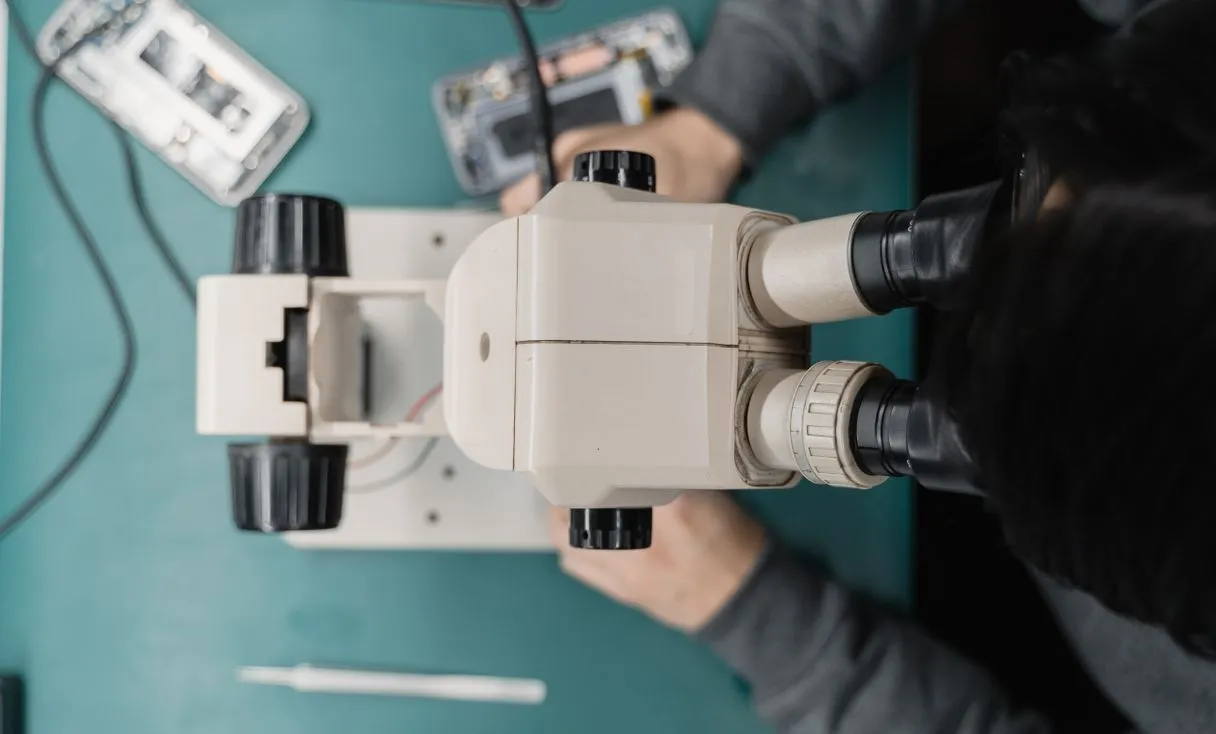 Técnico usando microscópio e ferramentas em bancada representando: Como contratar o primeiro técnico de celular: teste e salário