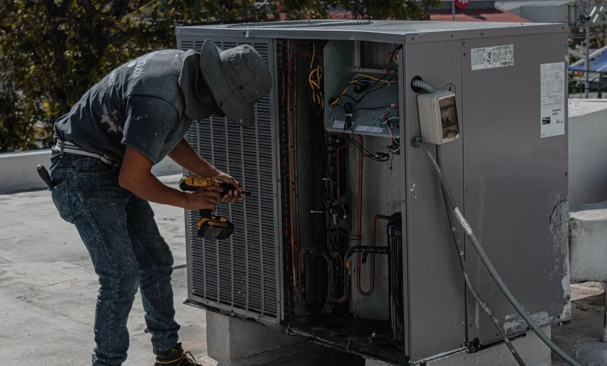 Técnico ajustando condensadora em telhado, ferramenta na mão, representando: Implantar controle de OS em 7 dias na refrigeração